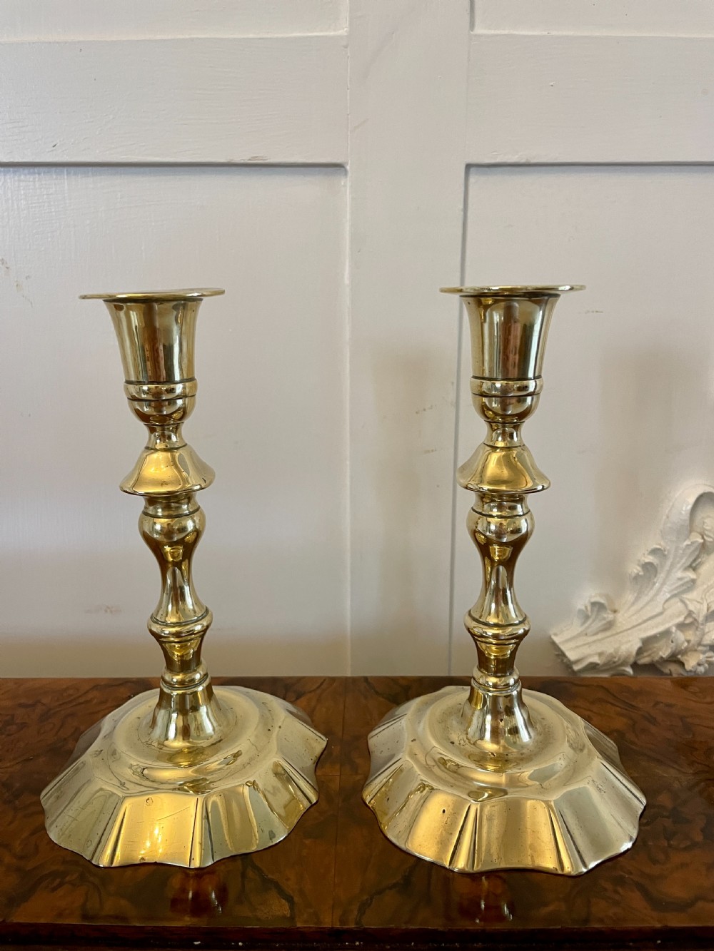 A pair of George III brass candlesticks featuring turned baluster stems and shaped scalloped bases.