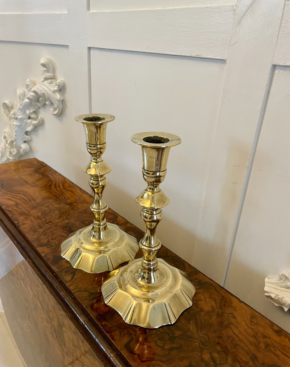 A pair of George III brass candlesticks featuring turned baluster stems and shaped scalloped bases. View III