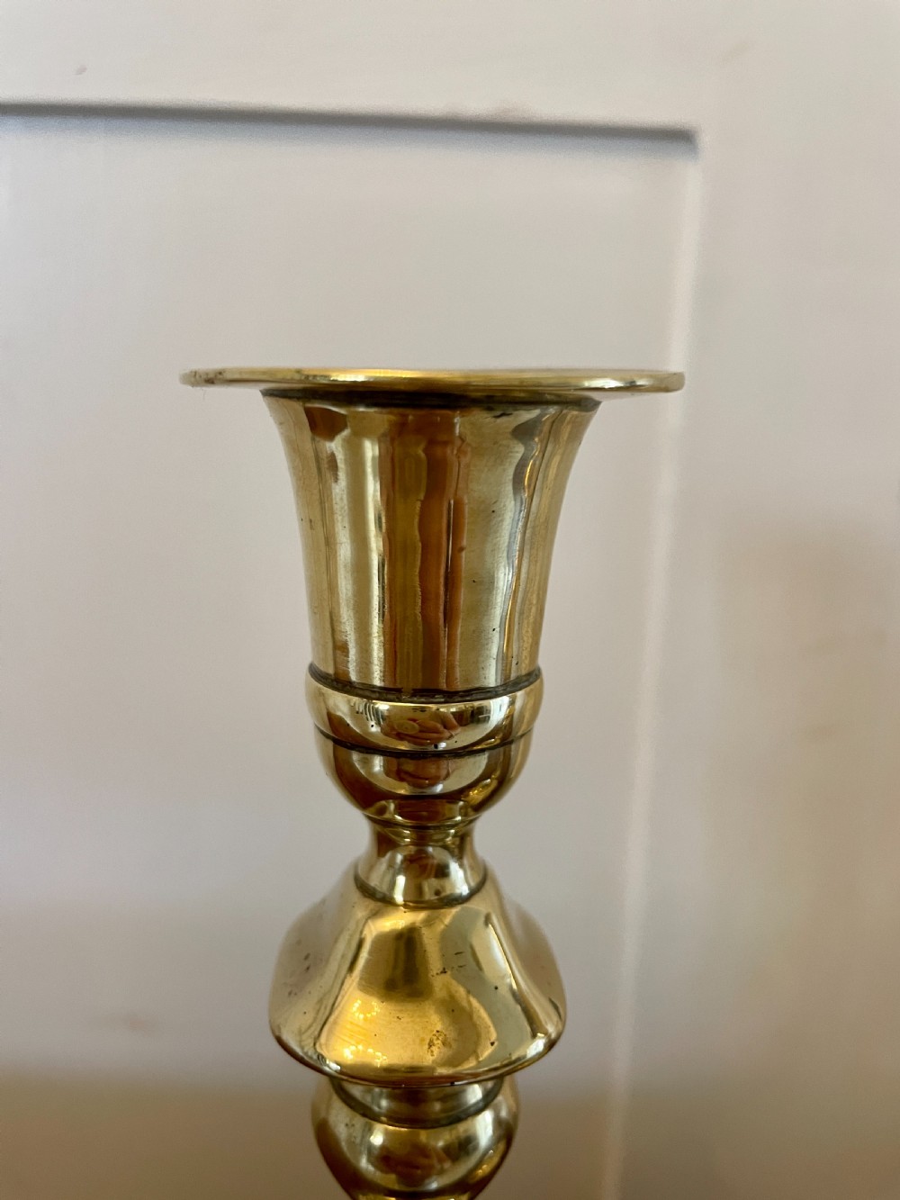 A pair of George III brass candlesticks featuring turned baluster stems and shaped scalloped bases. View X