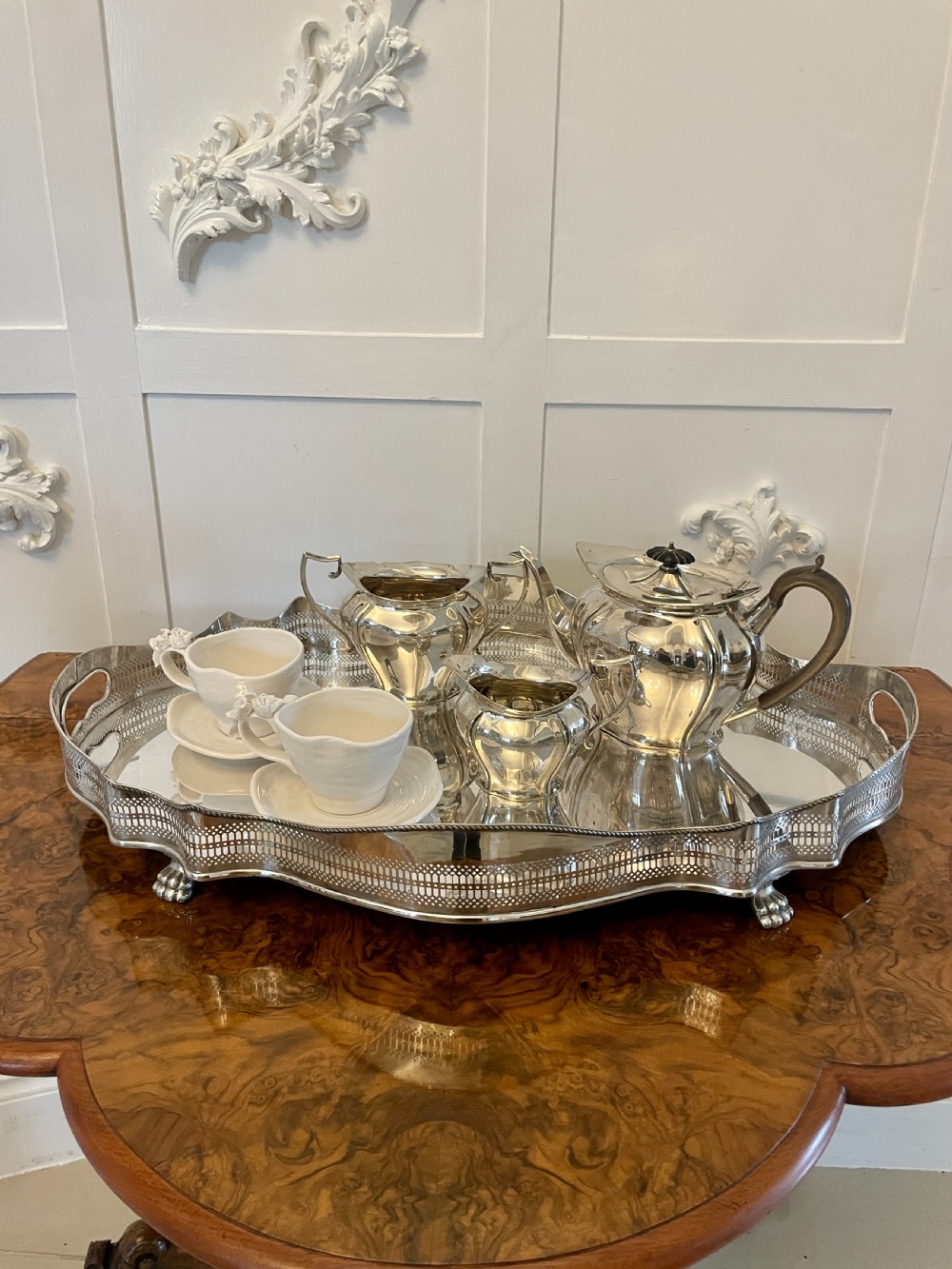 A three-piece Edwardian silver-plated tea set featuring a fluted teapot with a dark wooden handle, a matching double-handled sugar bowl, and a cream jug. View II