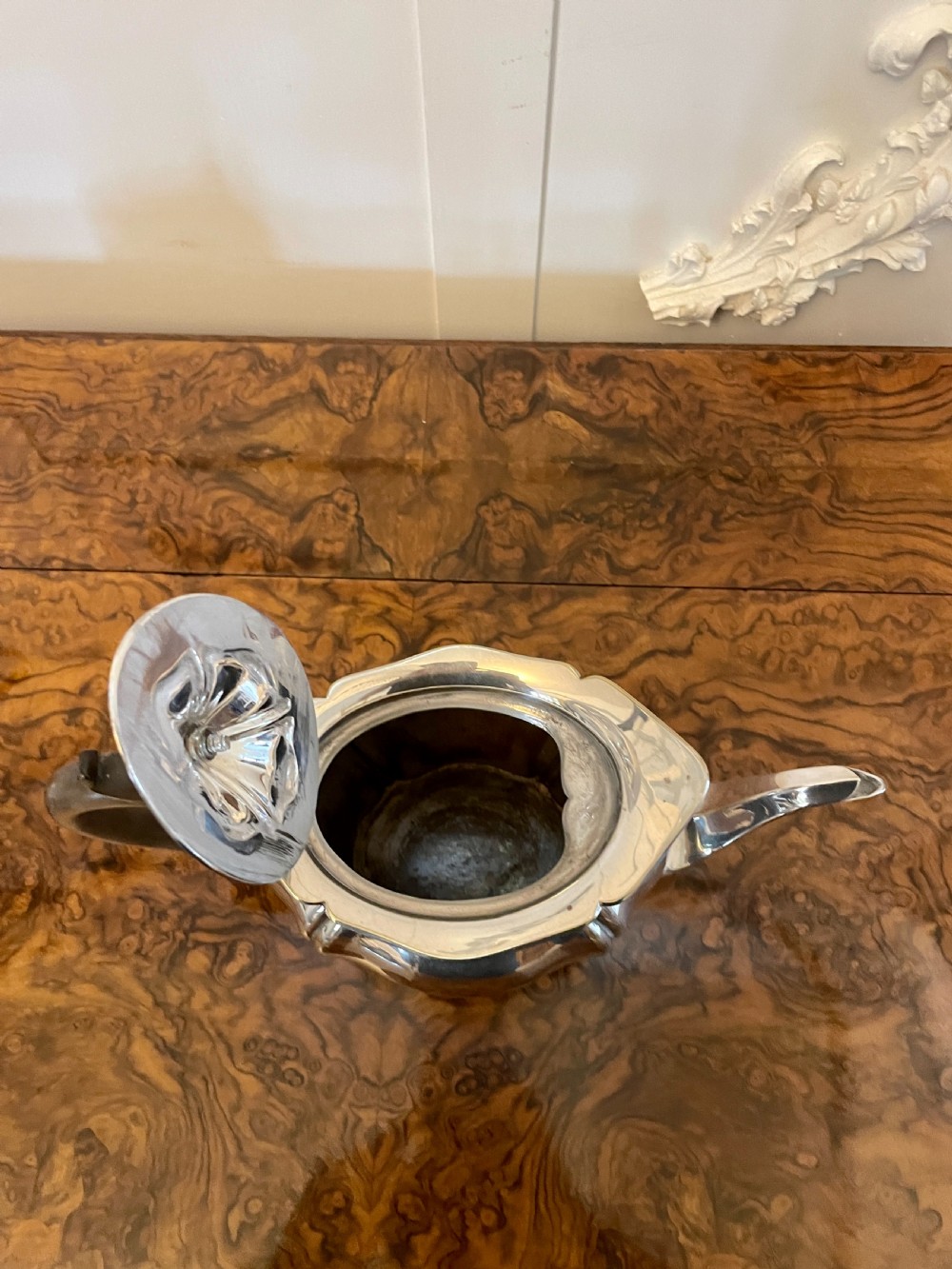 A three-piece Edwardian silver-plated tea set featuring a fluted teapot with a dark wooden handle, a matching double-handled sugar bowl, and a cream jug. View V
