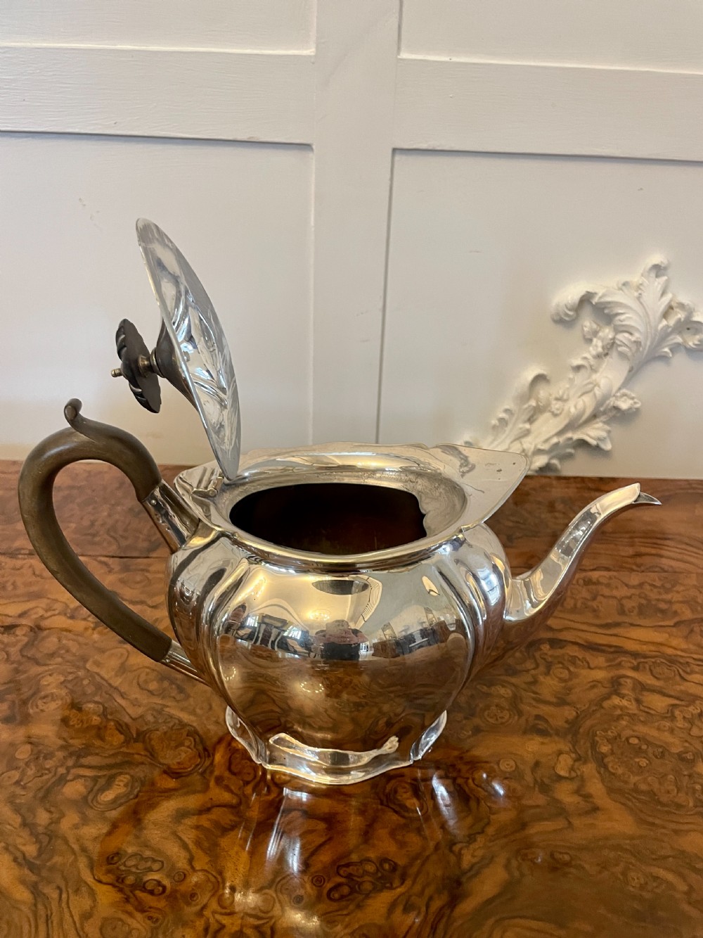 A three-piece Edwardian silver-plated tea set featuring a fluted teapot with a dark wooden handle, a matching double-handled sugar bowl, and a cream jug. View VI