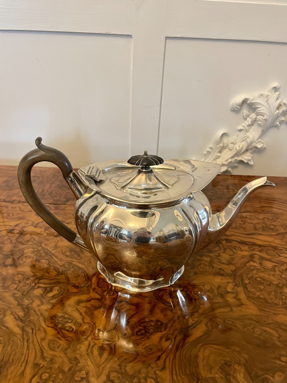 A three-piece Edwardian silver-plated tea set featuring a fluted teapot with a dark wooden handle, a matching double-handled sugar bowl, and a cream jug. View VII