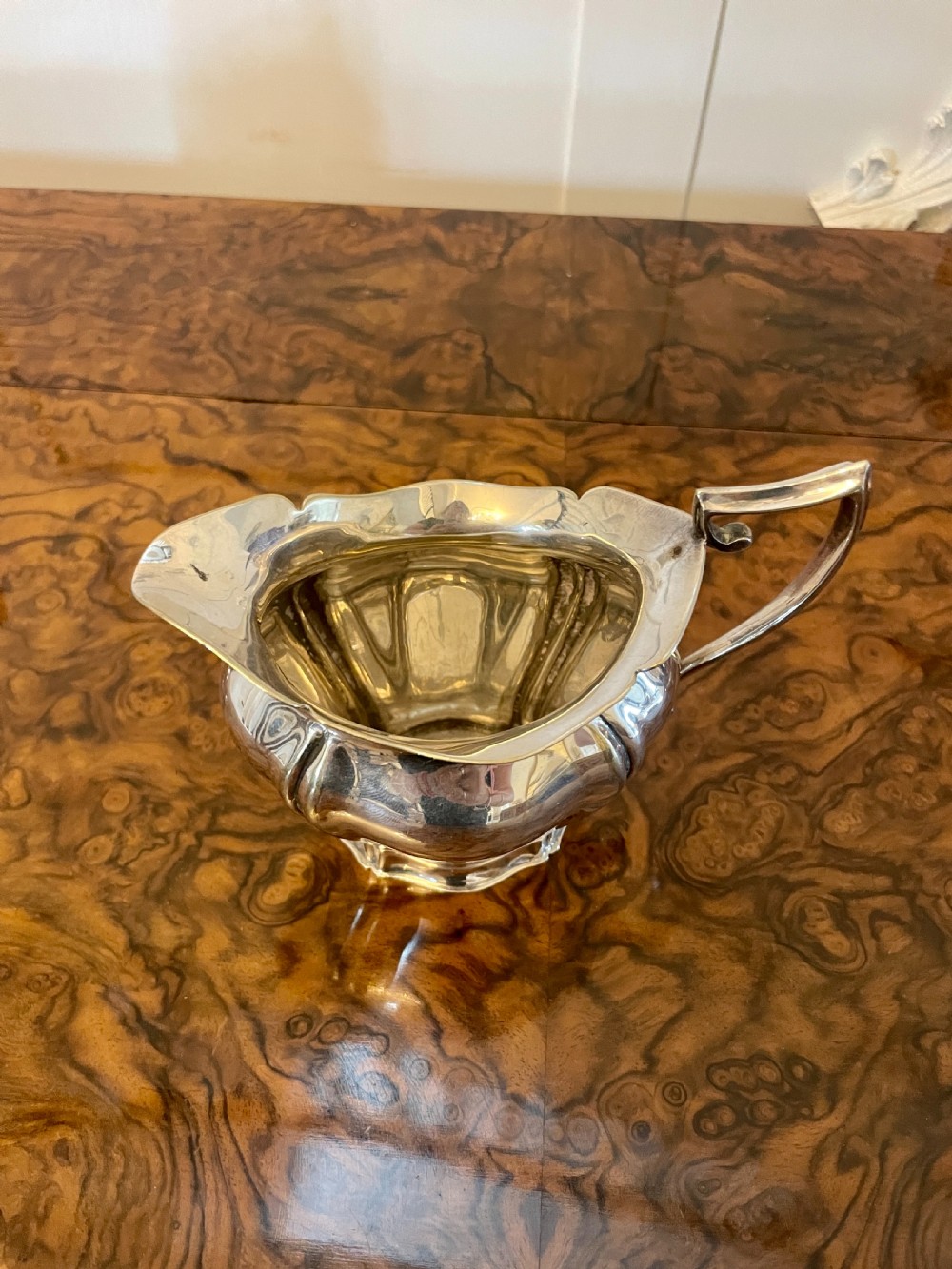 A three-piece Edwardian silver-plated tea set featuring a fluted teapot with a dark wooden handle, a matching double-handled sugar bowl, and a cream jug. View IX
