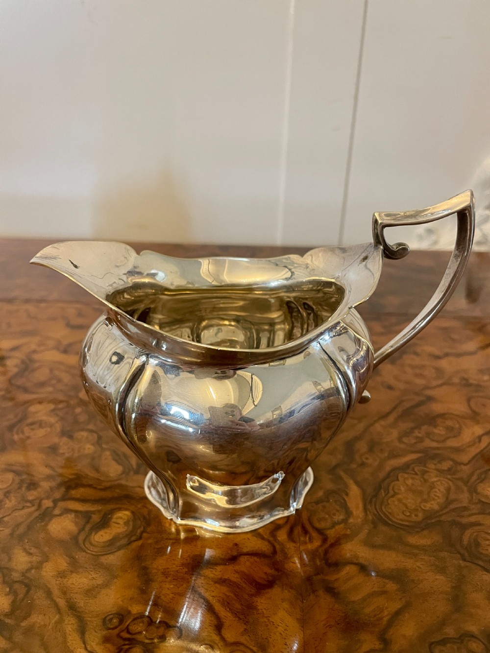 A three-piece Edwardian silver-plated tea set featuring a fluted teapot with a dark wooden handle, a matching double-handled sugar bowl, and a cream jug. View X