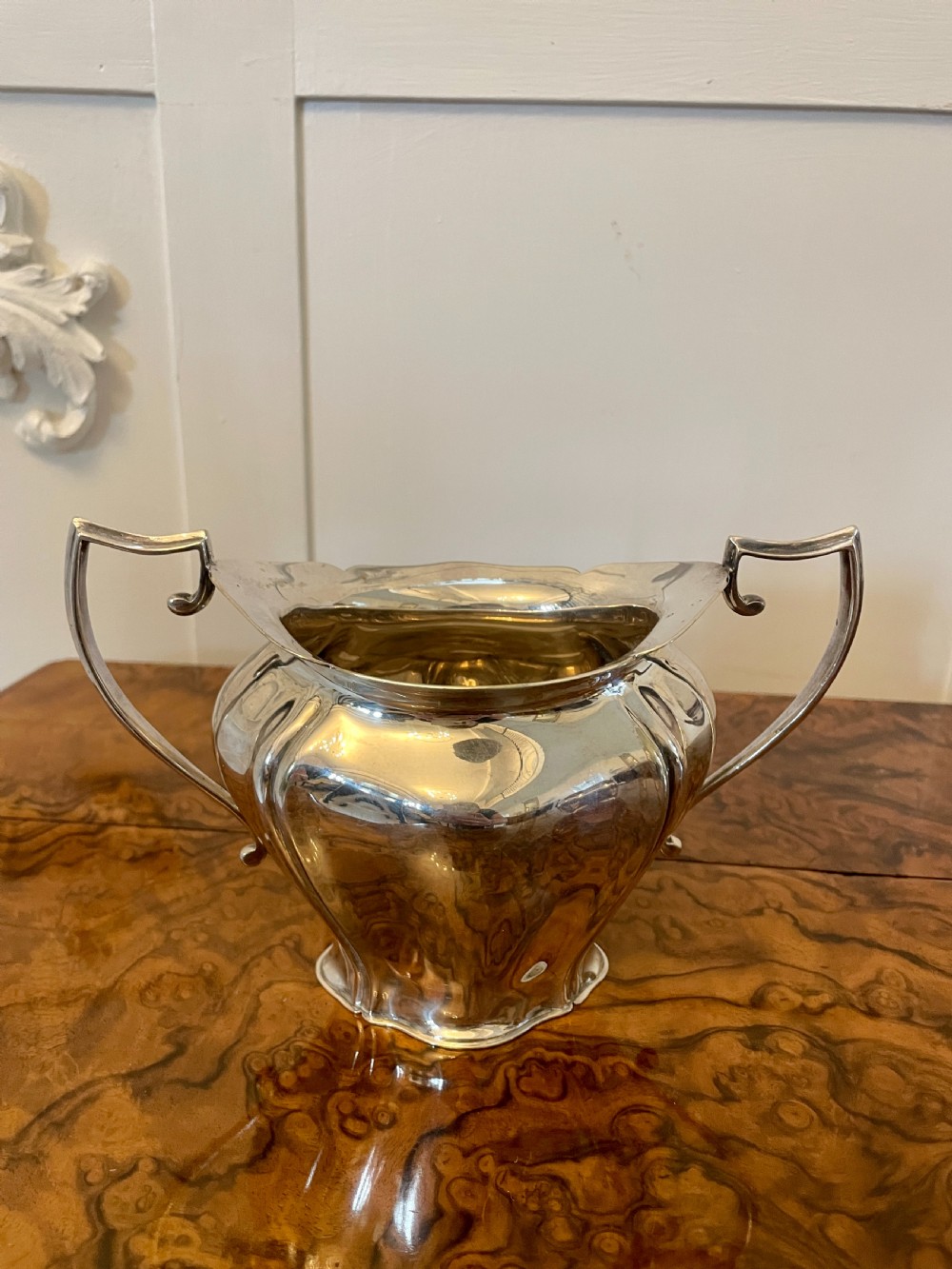 A three-piece Edwardian silver-plated tea set featuring a fluted teapot with a dark wooden handle, a matching double-handled sugar bowl, and a cream jug. View XI