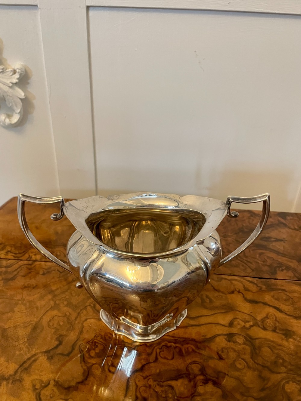 A three-piece Edwardian silver-plated tea set featuring a fluted teapot with a dark wooden handle, a matching double-handled sugar bowl, and a cream jug. View XII