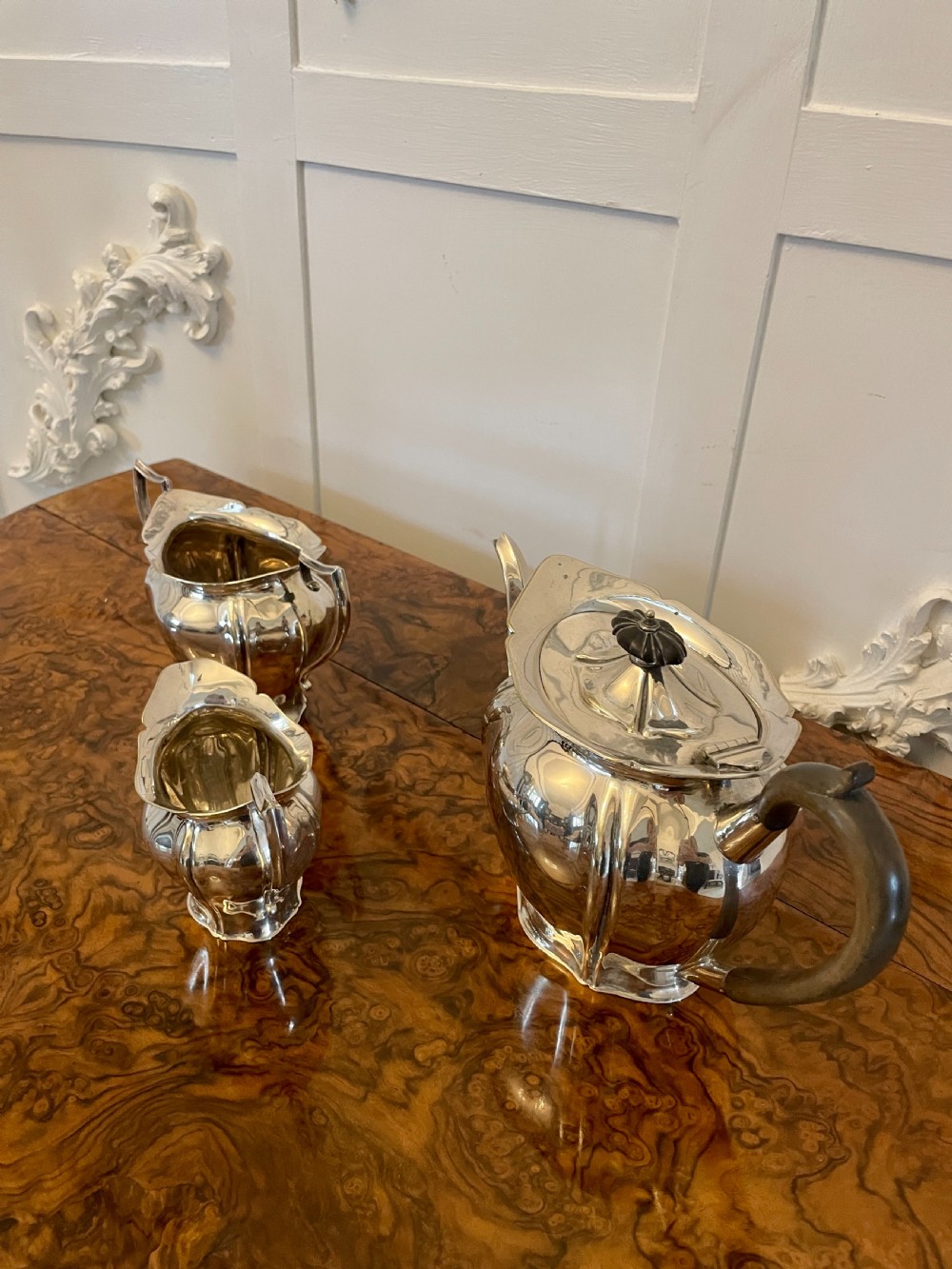 A three-piece Edwardian silver-plated tea set featuring a fluted teapot with a dark wooden handle, a matching double-handled sugar bowl, and a cream jug. View XIV