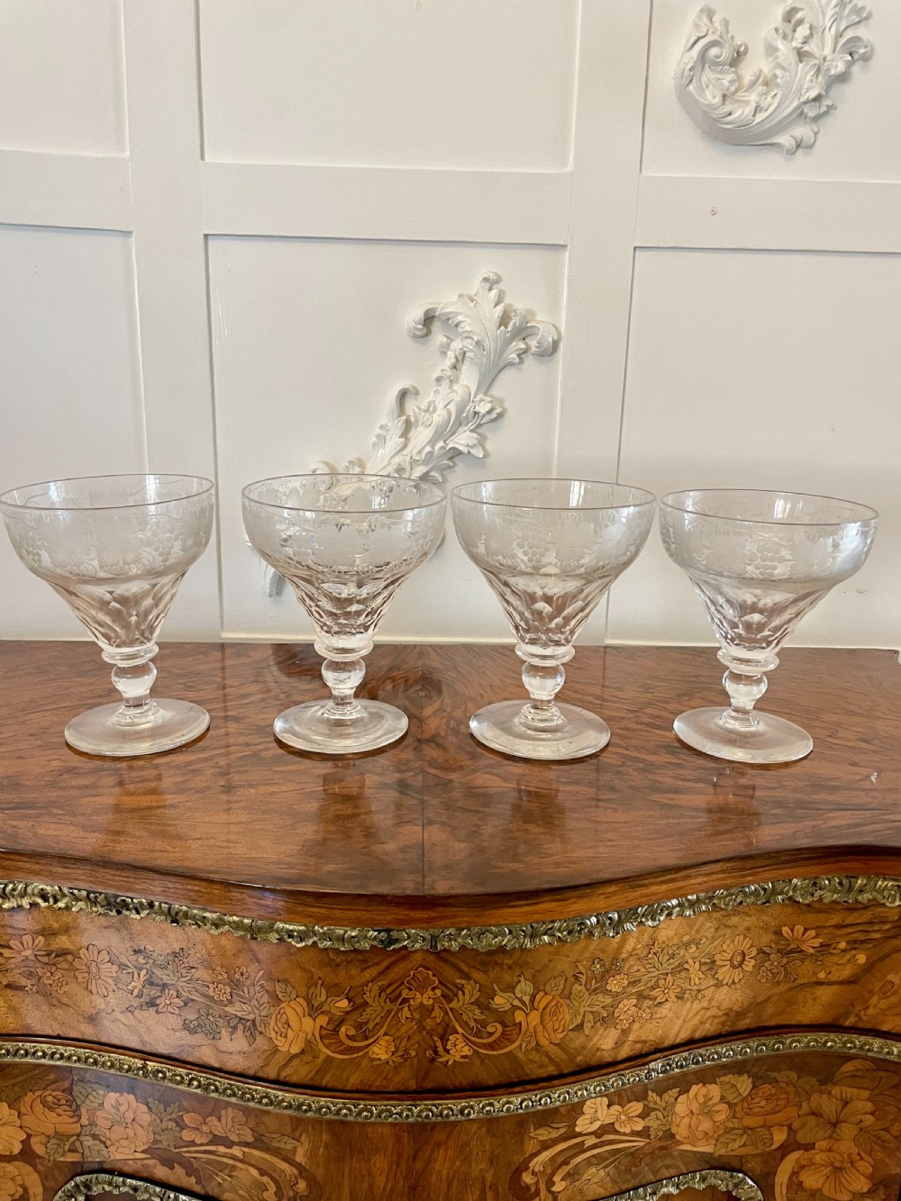 A set of four clear Victorian stemware glasses featuring detailed wheel-engraved grapevine motifs around the bowl and cut glass facets above a circular foot.
