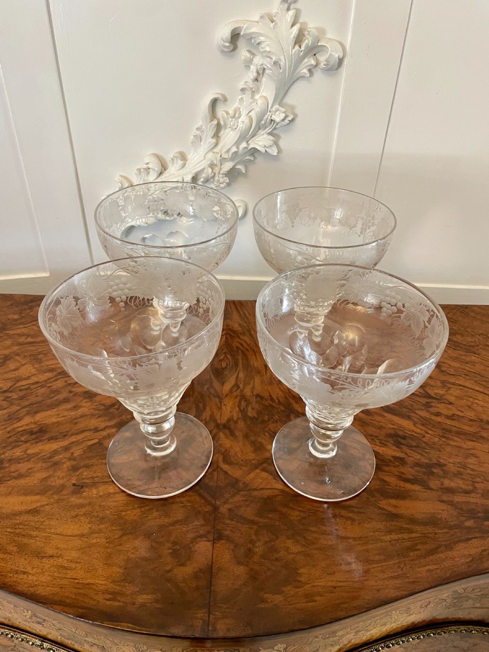 A set of four clear Victorian stemware glasses featuring detailed wheel-engraved grapevine motifs around the bowl and cut glass facets above a circular foot. View V
