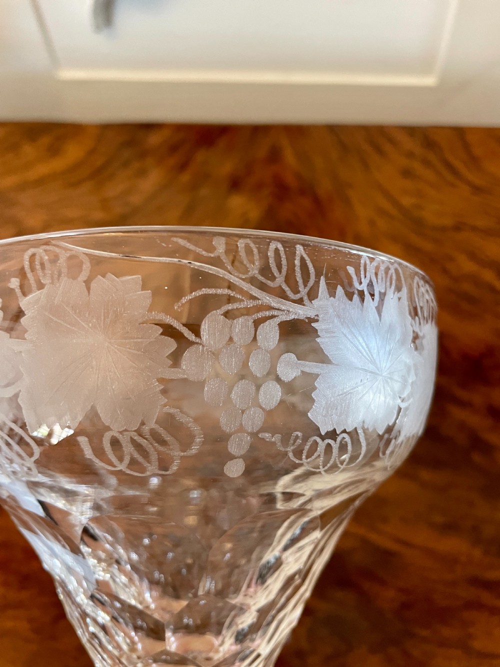 A set of four clear Victorian stemware glasses featuring detailed wheel-engraved grapevine motifs around the bowl and cut glass facets above a circular foot. View VII