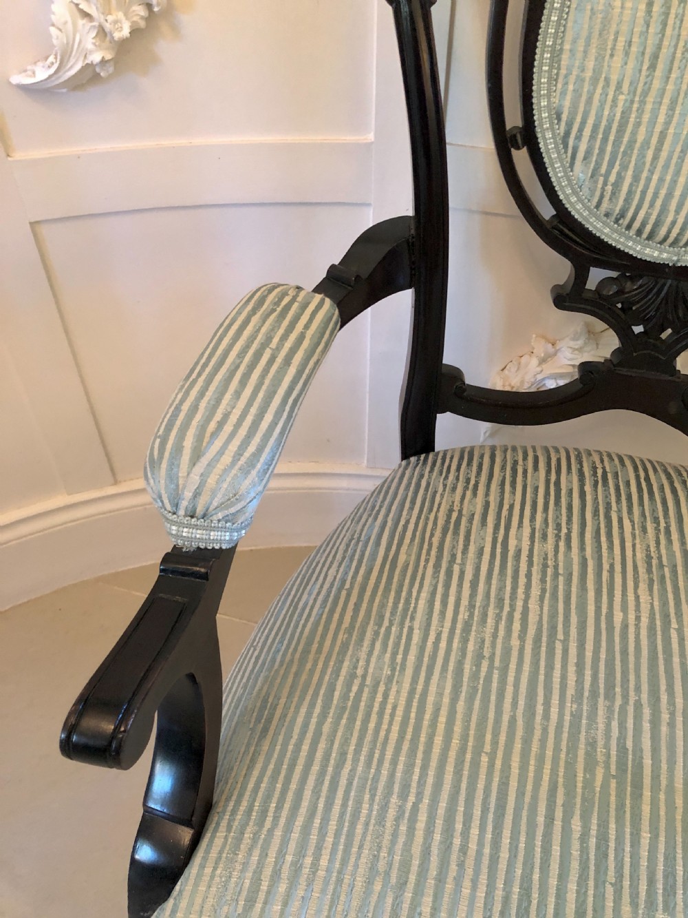 A pair of Victorian carved black lacquered open armchairs featuring oval padded backrests, curved padded arms, pale green striped fabric, and cabriole legs with brass castors. View VI
