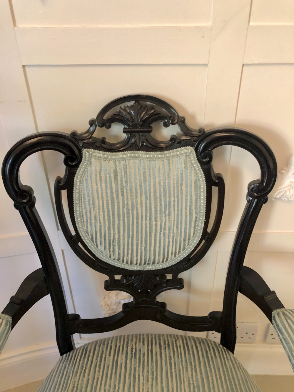 A pair of Victorian carved black lacquered open armchairs featuring oval padded backrests, curved padded arms, pale green striped fabric, and cabriole legs with brass castors. View VII