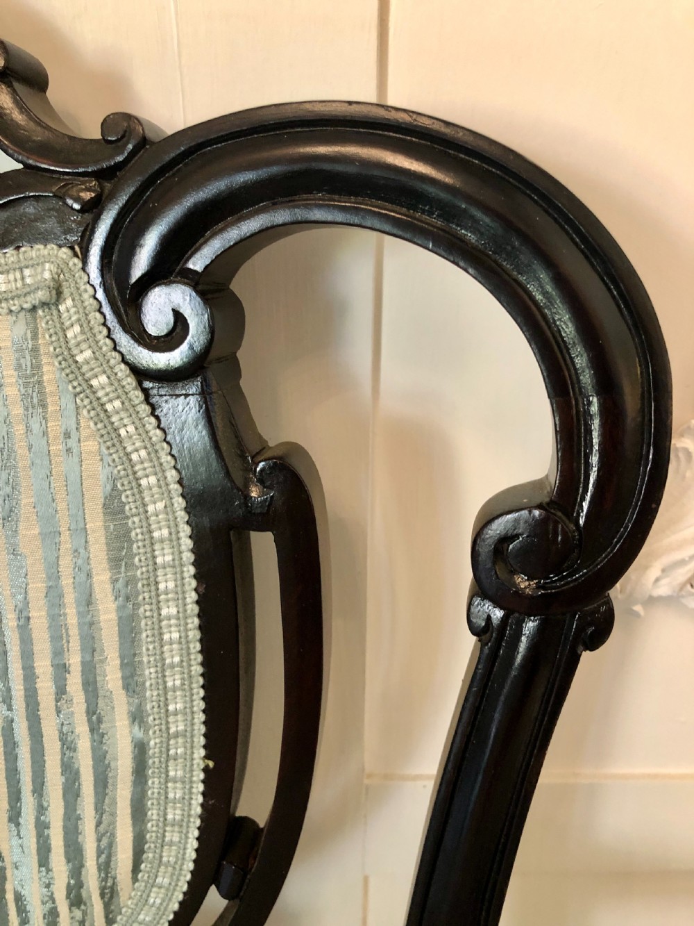 A pair of Victorian carved black lacquered open armchairs featuring oval padded backrests, curved padded arms, pale green striped fabric, and cabriole legs with brass castors. View VIII