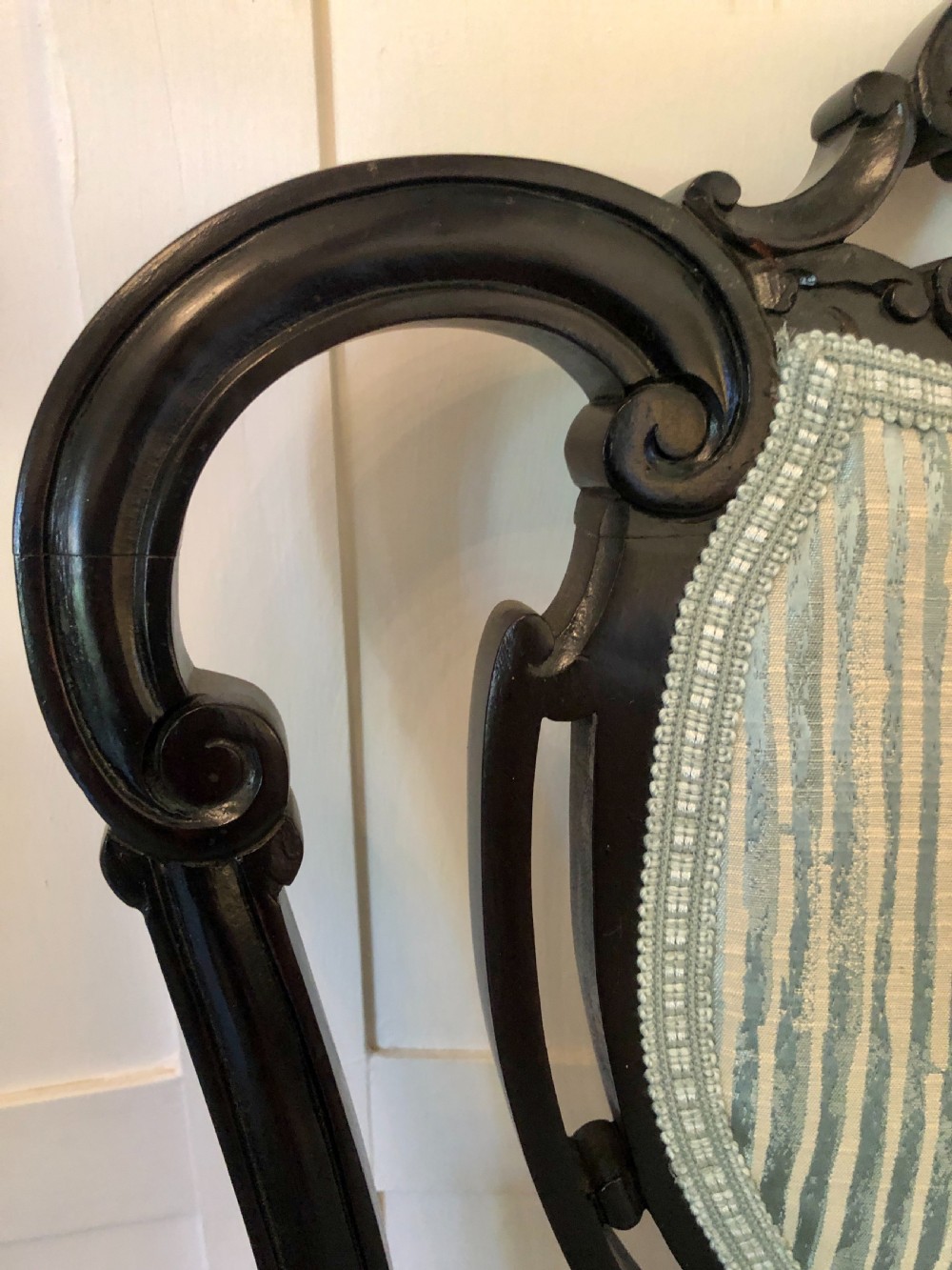 A pair of Victorian carved black lacquered open armchairs featuring oval padded backrests, curved padded arms, pale green striped fabric, and cabriole legs with brass castors. View X