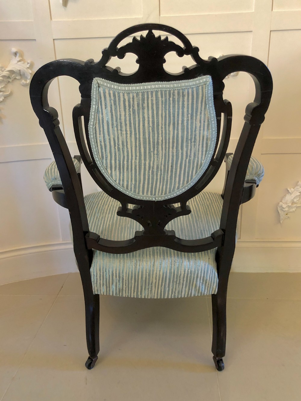 A pair of Victorian carved black lacquered open armchairs featuring oval padded backrests, curved padded arms, pale green striped fabric, and cabriole legs with brass castors. View XI