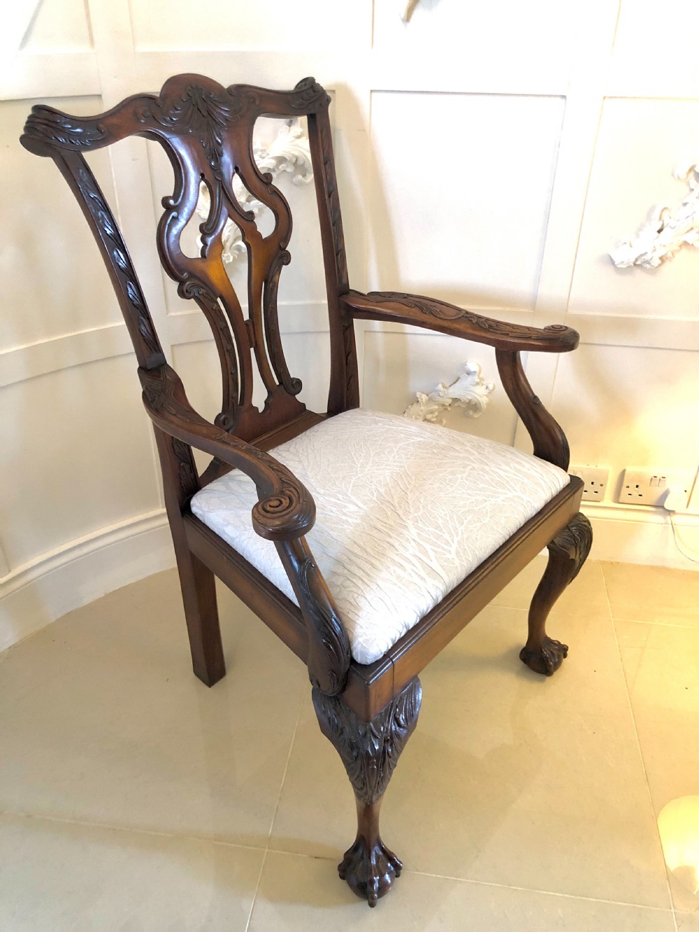 A carved mahogany Chippendale style desk armchair featuring a pierced back splat, scrolled armrests, light upholstered seat, and cabriole legs ending in ball and claw feet.