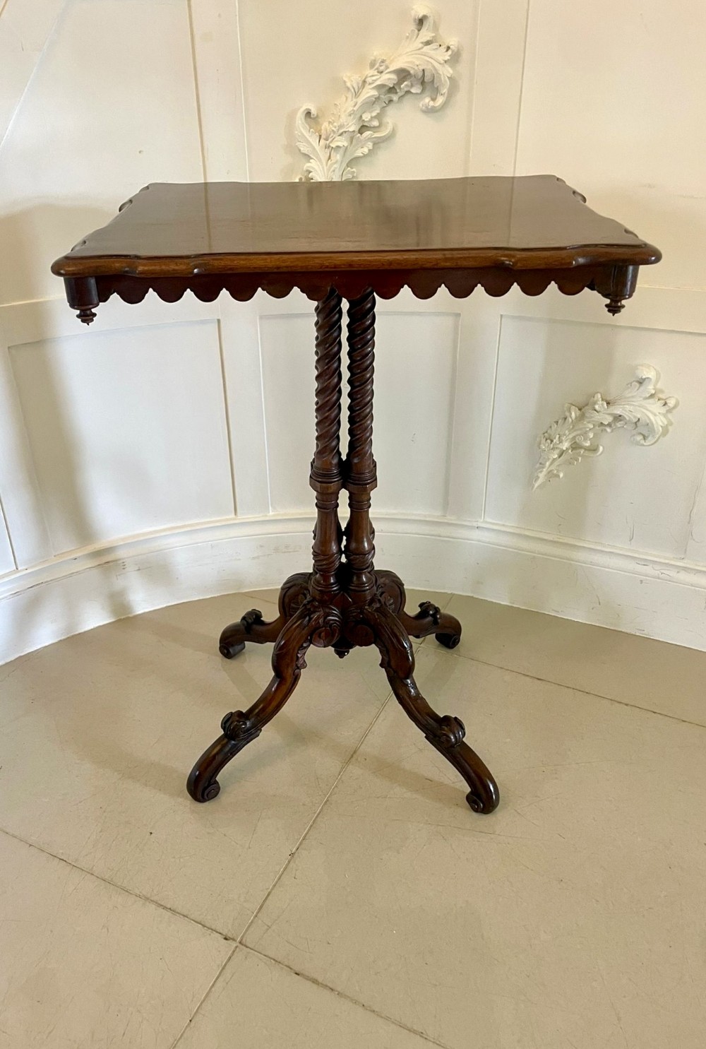 An antique Victorian walnut lamp table featuring a shaped rectangular top, twin barley-twist columns, and a carved tripod base.