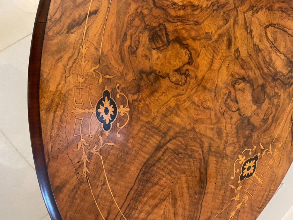 An antique Victorian oval centre table featuring book-matched burr walnut veneer with intricate floral inlay, supported by a carved central pedestal and four splayed legs on castors. View XI