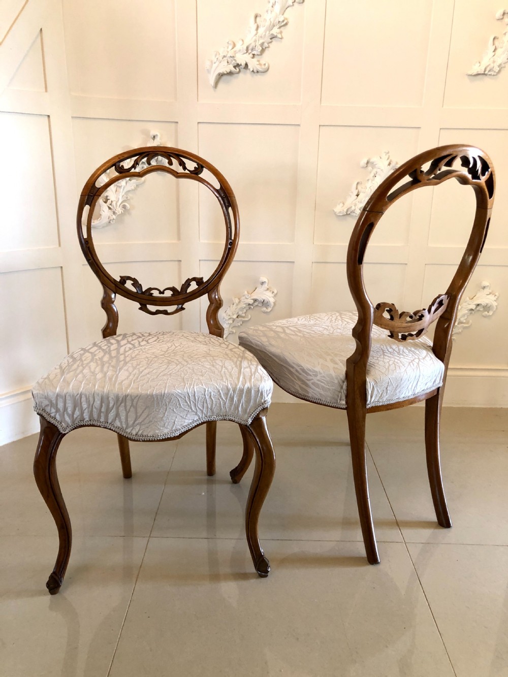 A set of six Victorian walnut dining chairs featuring carved circular balloon backs, cabriole front legs, and light silver patterned upholstered seats. View VI