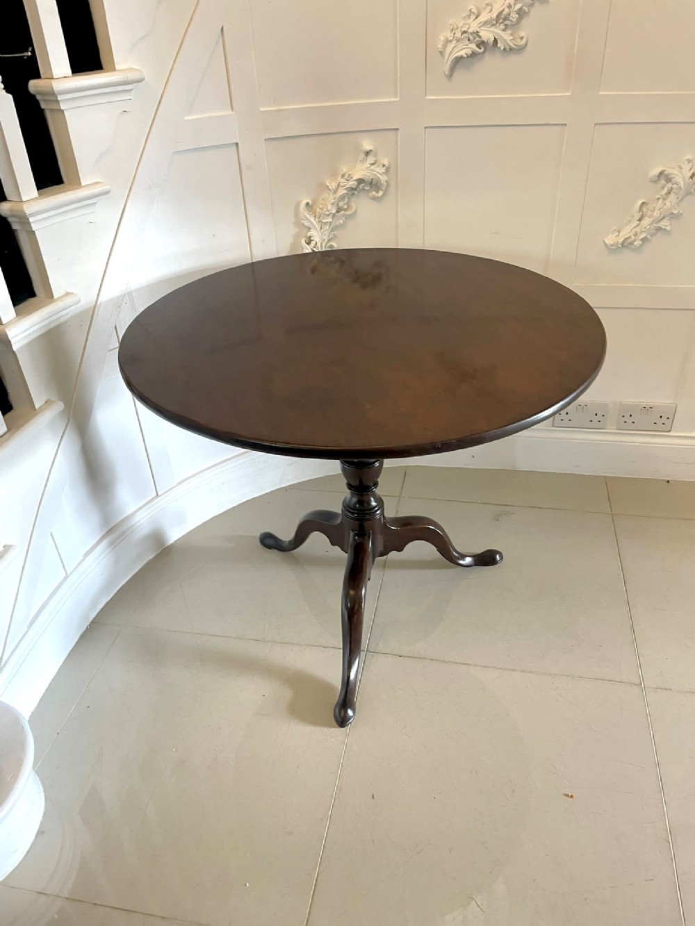 An antique round mahogany tripod table featuring a polished circular top atop a turned central column and three cabriole legs.