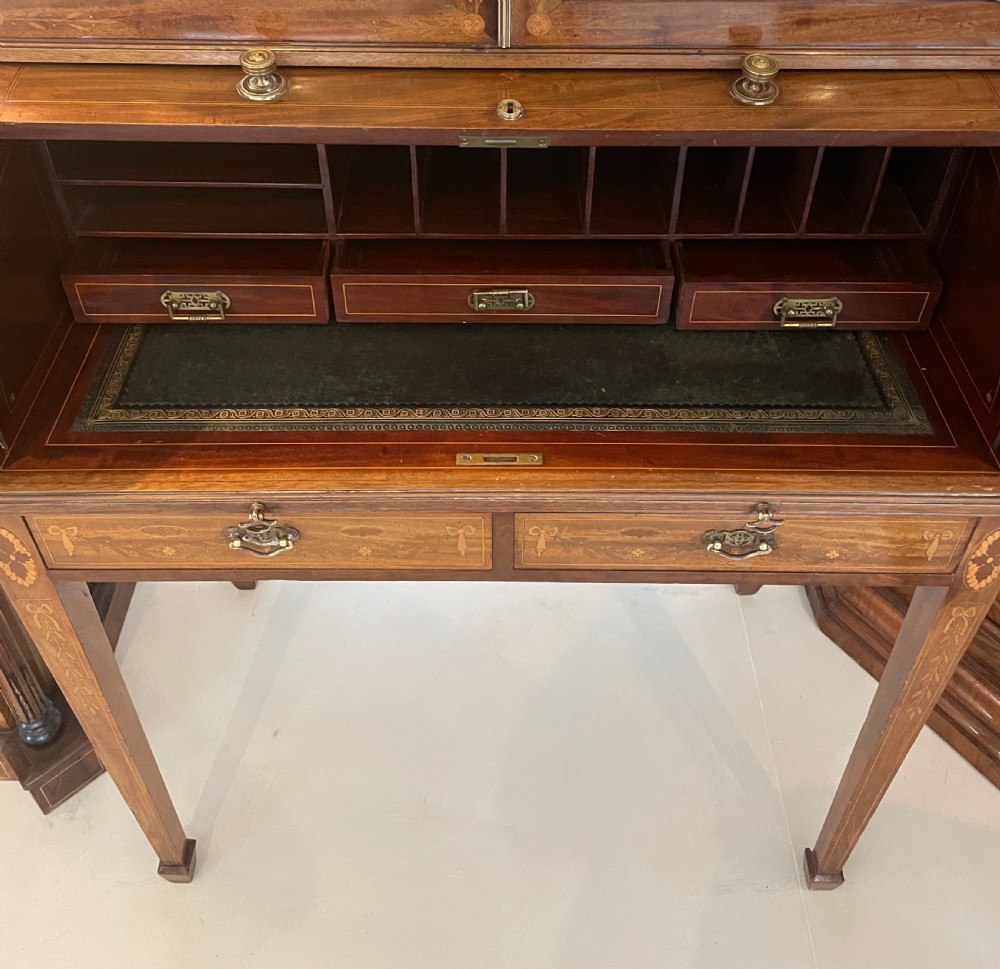 An antique mahogany cylinder bureau bookcase featuring a broken arch swan-neck pediment, twin glazed doors, floral marquetry inlay, and tapered legs. View XXIII