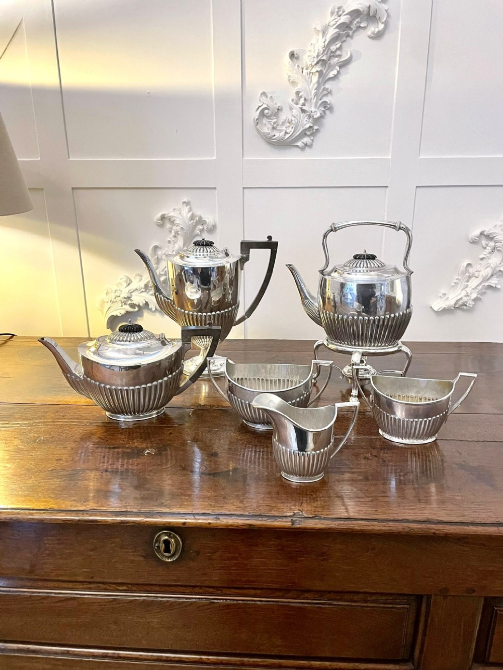 A six-piece Edwardian silver-plated tea and coffee service featuring half-fluted lower bodies and angular handles on a wooden surface.