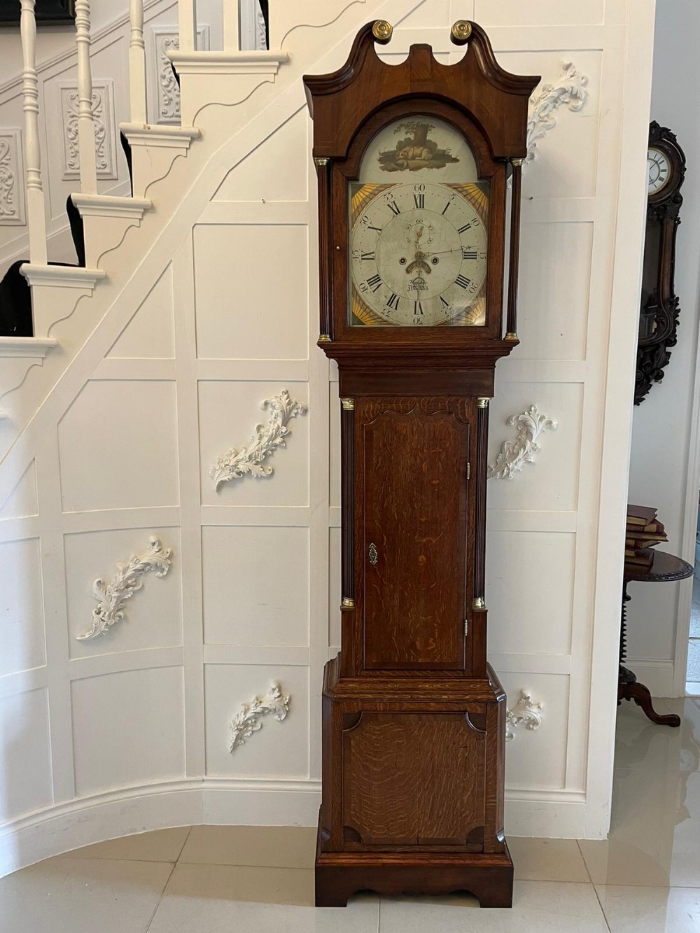 A George III oak longcase clock featuring a swan-neck pediment hood, an arched painted dial displaying Roman numerals, and fluted quarter columns.