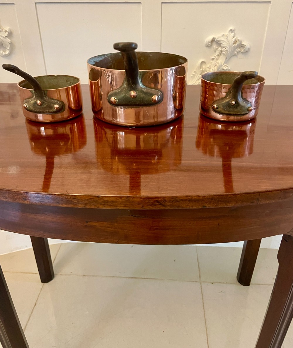 A set of three graduated Victorian copper saucepans featuring dark iron handles resting on a polished wooden surface. View II