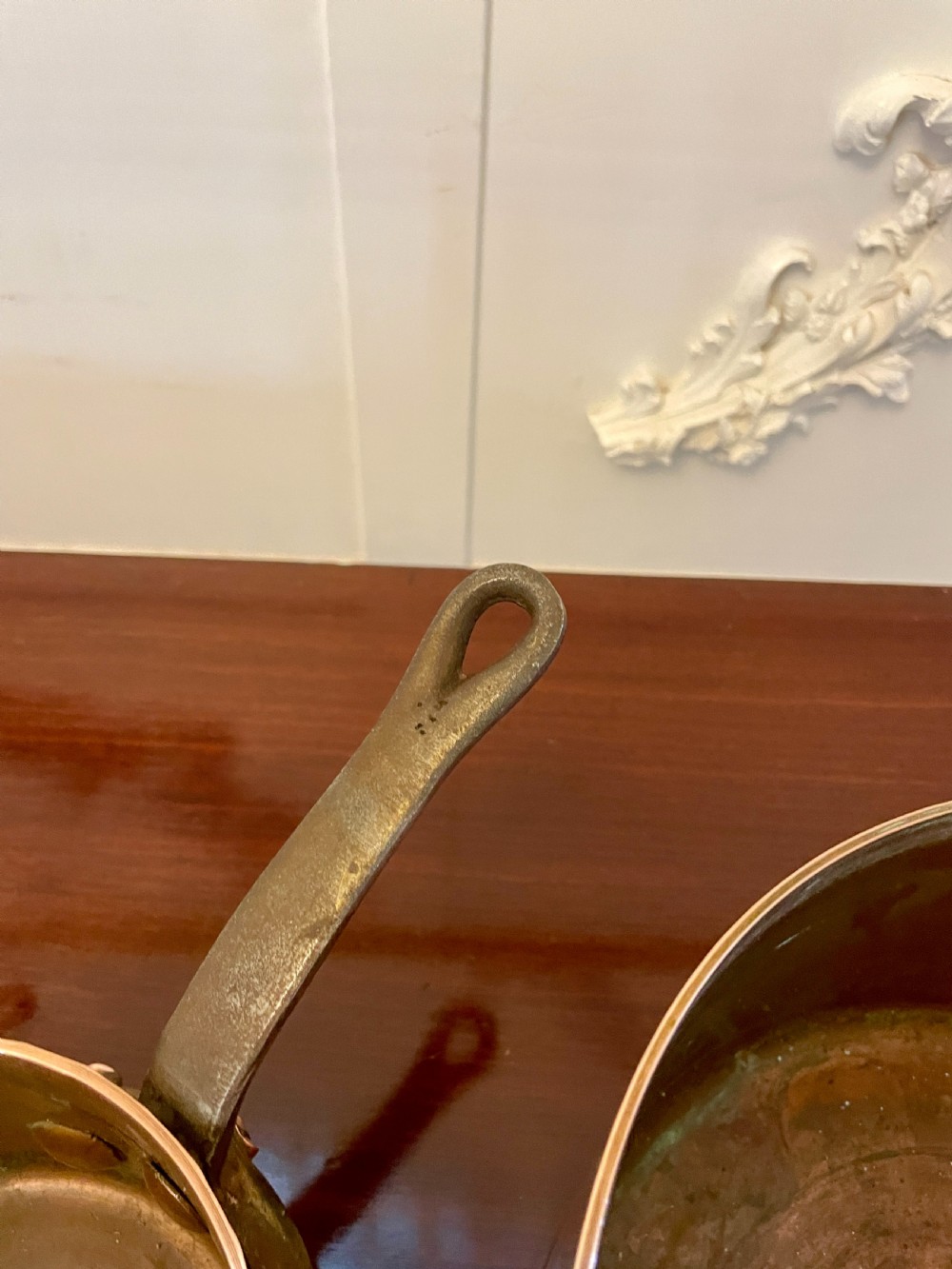 A set of three graduated Victorian copper saucepans featuring dark iron handles resting on a polished wooden surface. View V