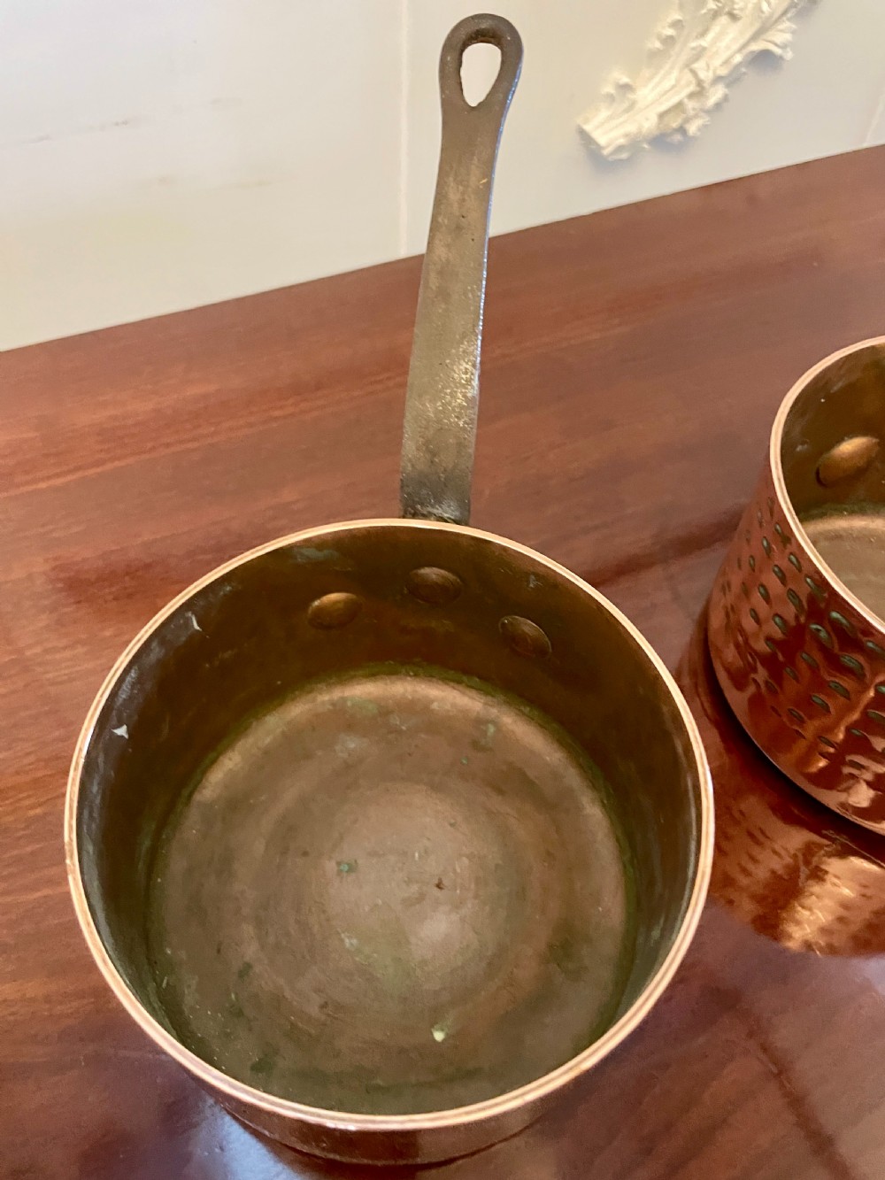 A set of three graduated Victorian copper saucepans featuring dark iron handles resting on a polished wooden surface. View VII