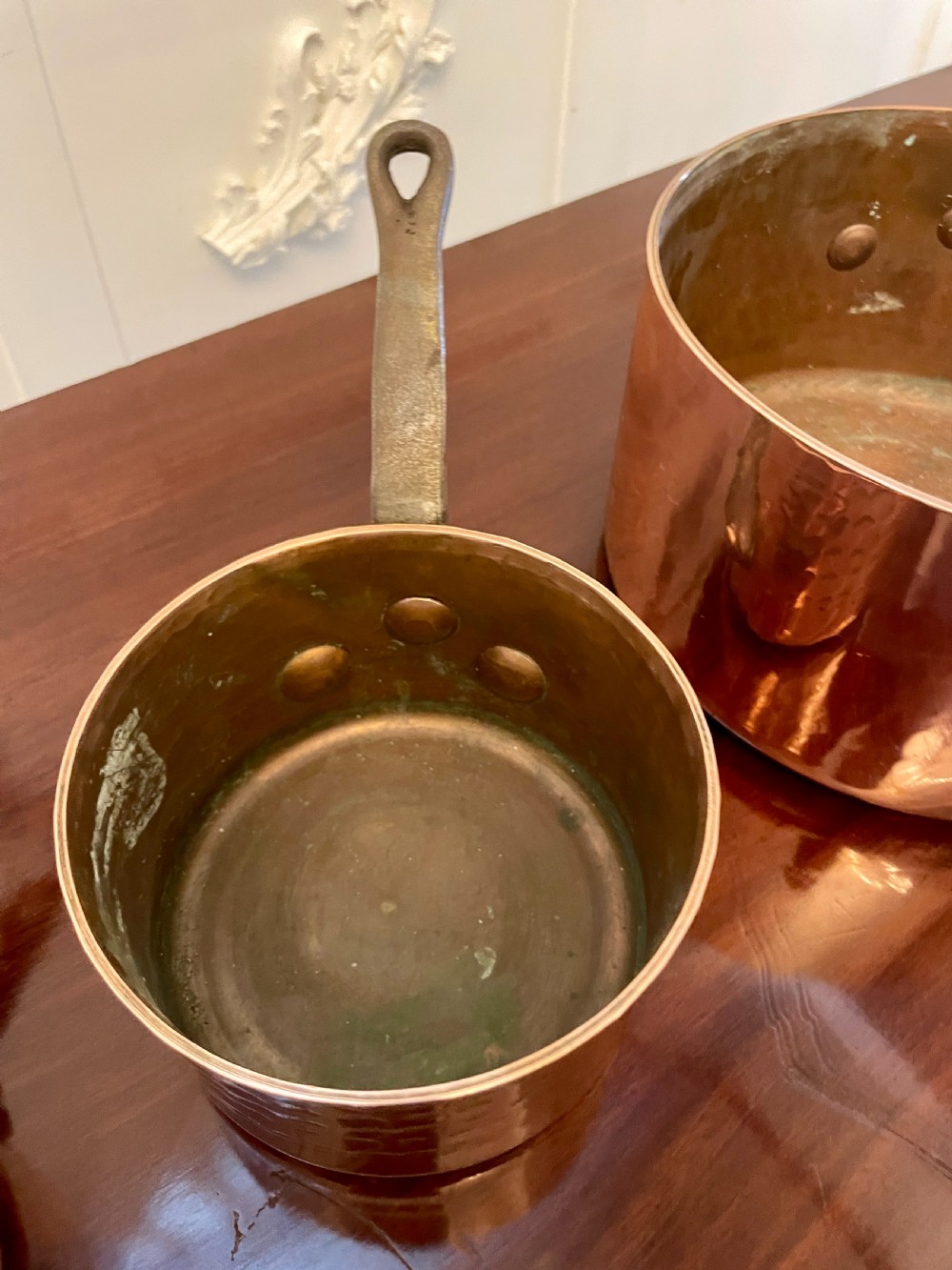 A set of three graduated Victorian copper saucepans featuring dark iron handles resting on a polished wooden surface. View VIII