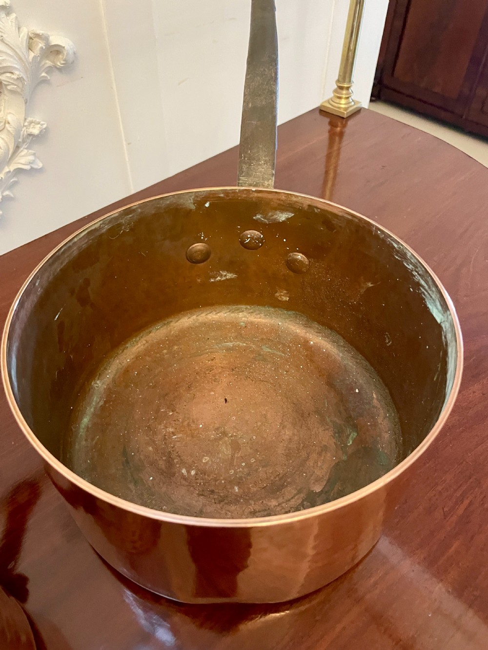 A set of three graduated Victorian copper saucepans featuring dark iron handles resting on a polished wooden surface. View IX