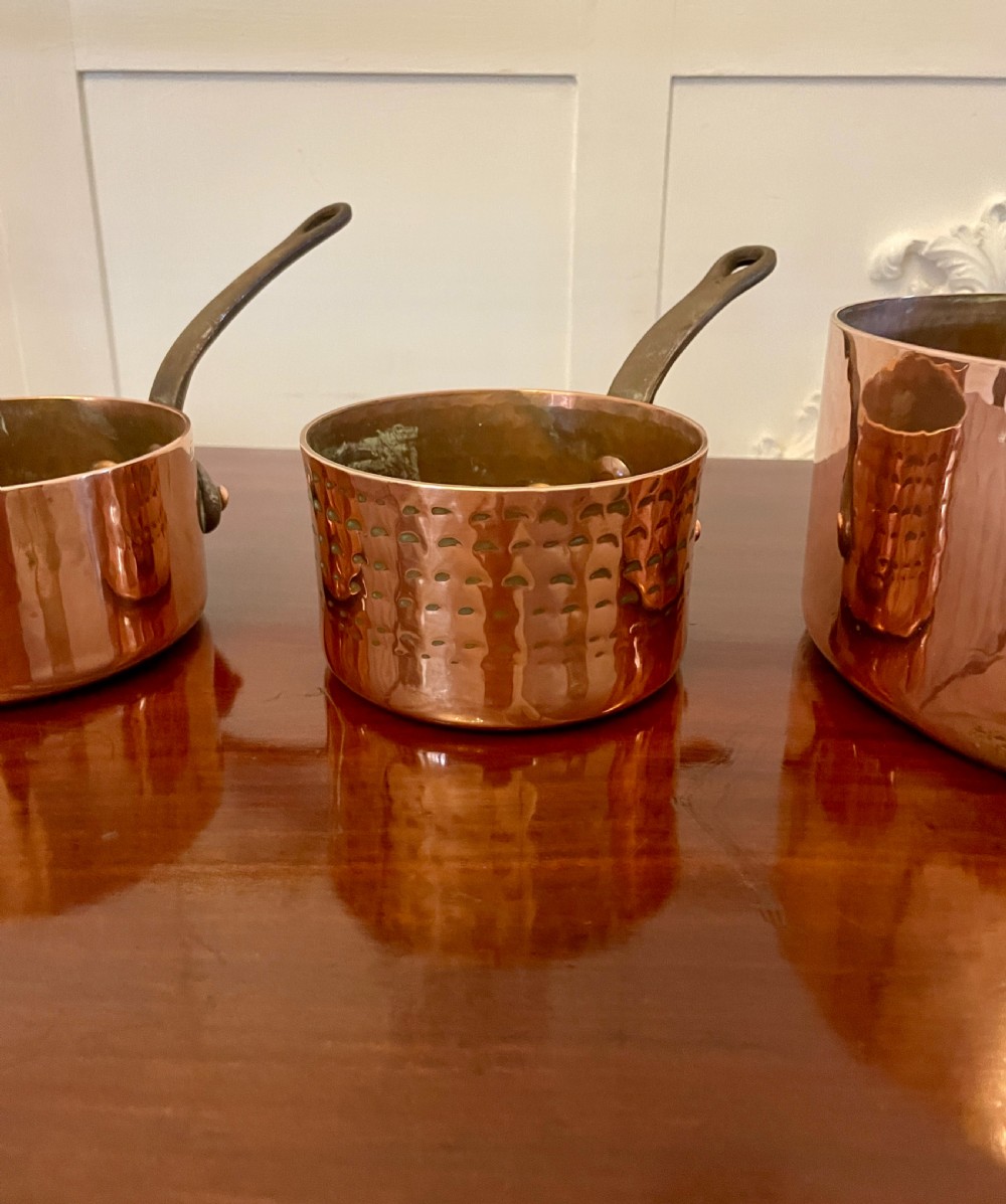 A set of three graduated Victorian copper saucepans featuring dark iron handles resting on a polished wooden surface. View XI
