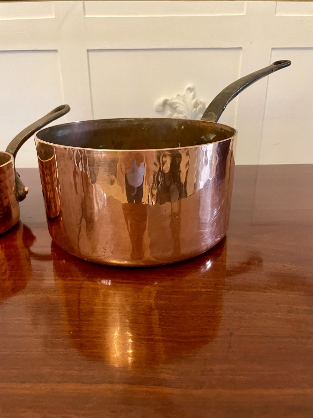 A set of three graduated Victorian copper saucepans featuring dark iron handles resting on a polished wooden surface. View XII