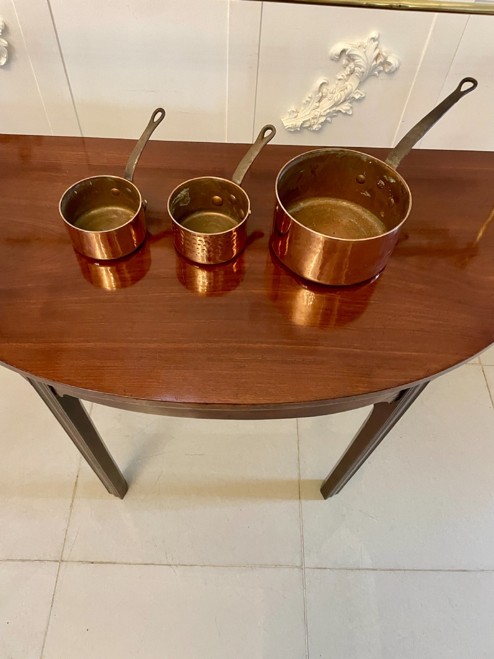 A set of three graduated Victorian copper saucepans featuring dark iron handles resting on a polished wooden surface. View XIII