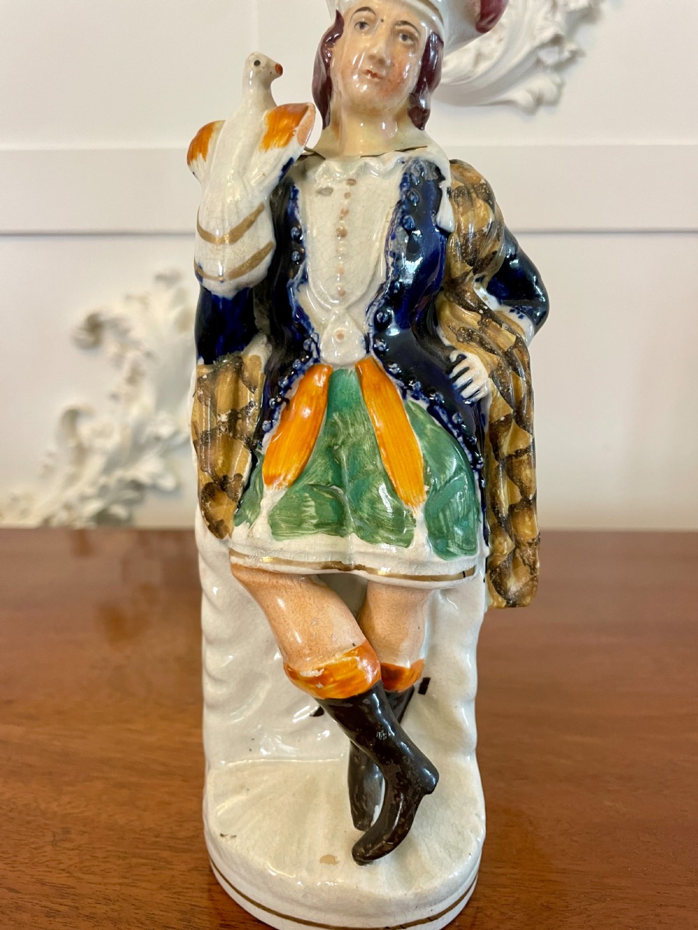 A Victorian Staffordshire earthenware flatback figure depicting a male standing character with a bird perched on his gloved hand, decorated in blue, green, orange, and white enamels.