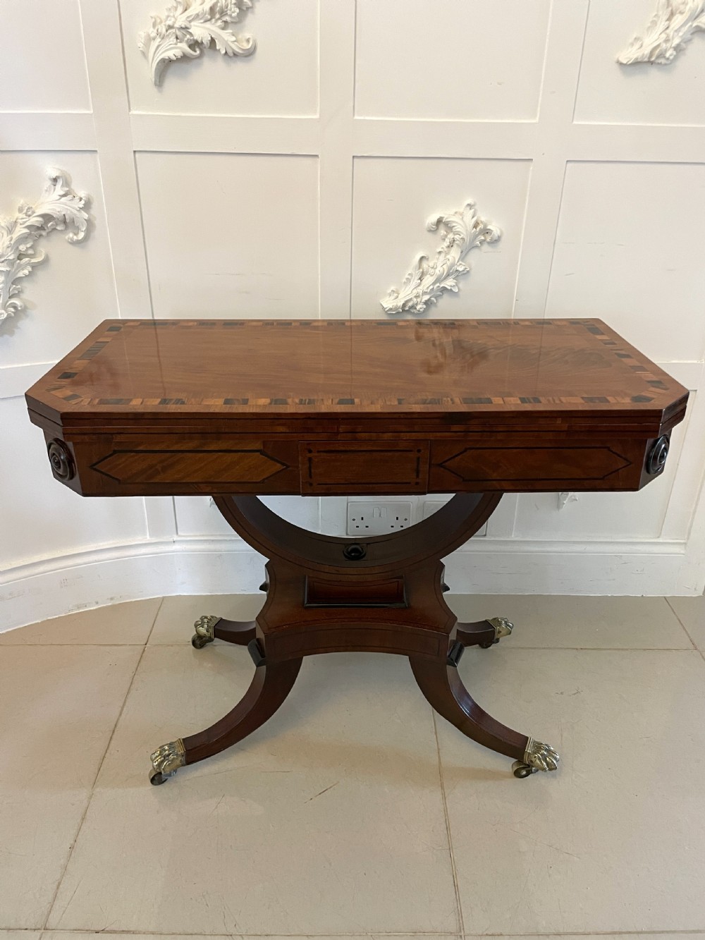 A Regency mahogany fold-over card table featuring crossbanded inlay, a central pedestal base, and four splayed legs with brass paw castors. View XVI