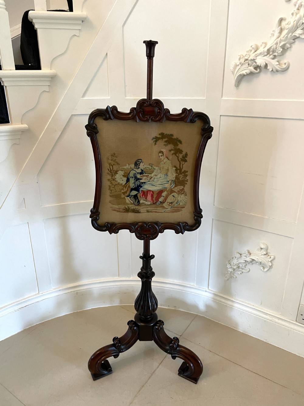 An antique Victorian carved rosewood pole screen featuring a framed tapestry panel depicting a pastoral scene, mounted on an adjustable central column with a tripod base.