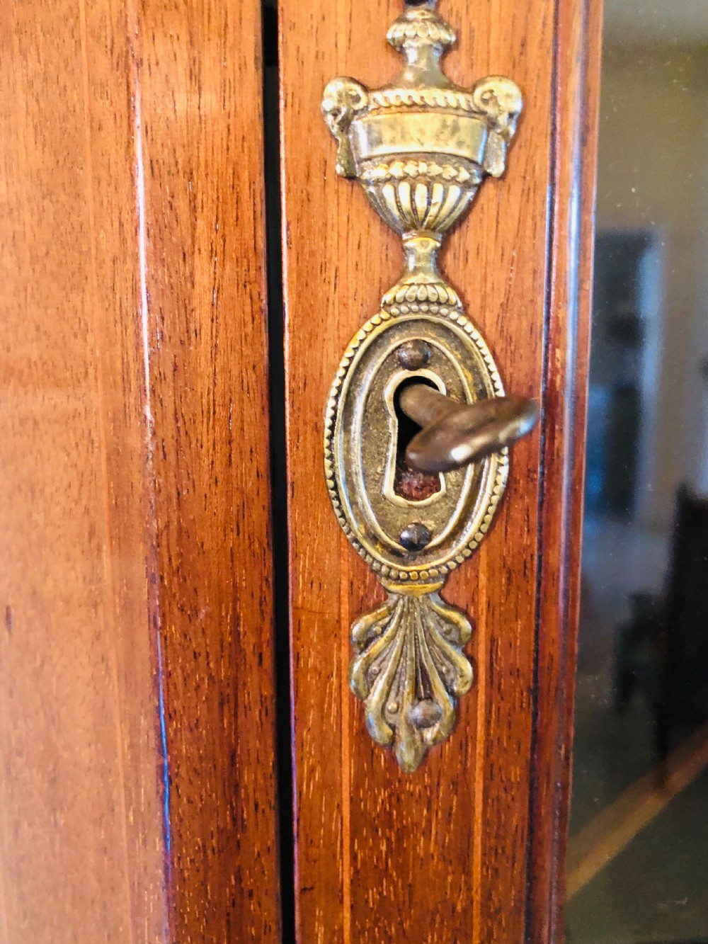 A tall Edwardian mahogany corner cupboard featuring a swan-neck pediment, astragal glazed upper door, and an inlaid lower door with an urn motif. View III