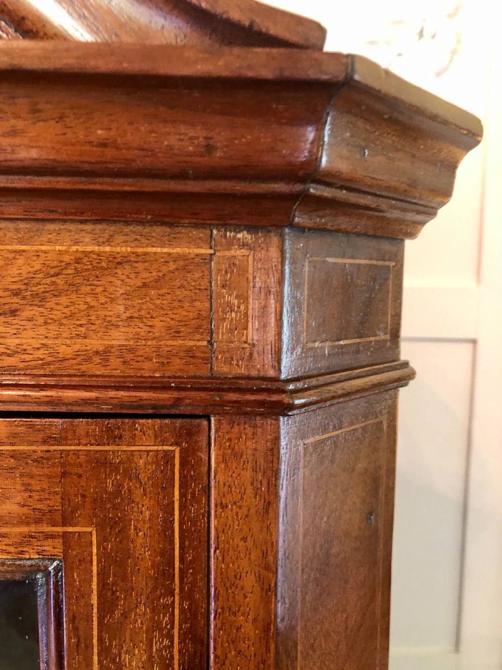 A tall Edwardian mahogany corner cupboard featuring a swan-neck pediment, astragal glazed upper door, and an inlaid lower door with an urn motif. View XII