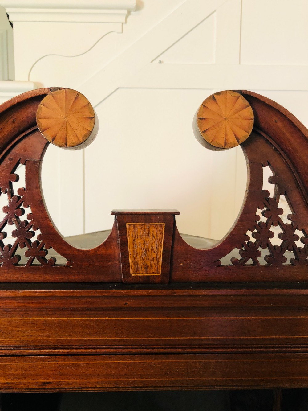 A tall Edwardian mahogany corner cupboard featuring a swan-neck pediment, astragal glazed upper door, and an inlaid lower door with an urn motif. View XVII