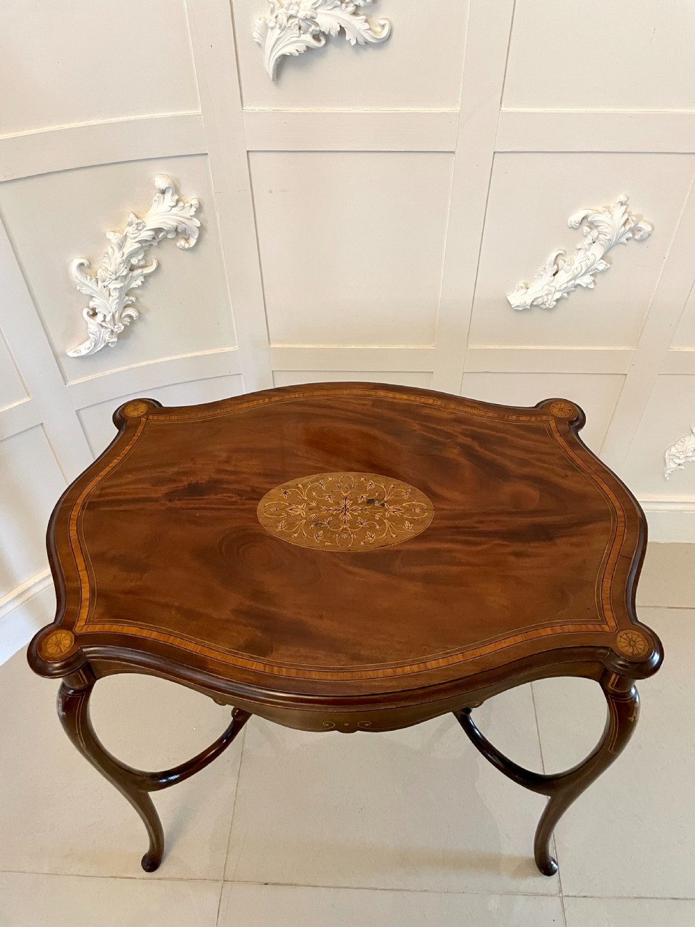 A Victorian mahogany centre table featuring a shaped serpentine top with floral marquetry inlay, slender cabriole legs, and a lower undertier. View X