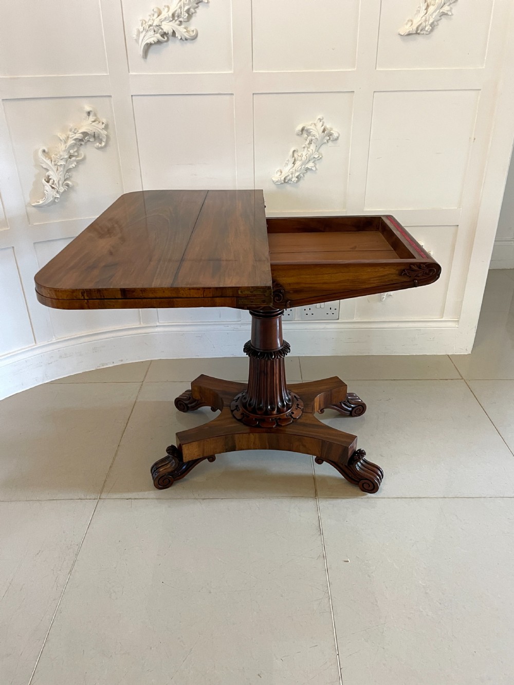 A Victorian rosewood fold-over card table featuring a turned central pedestal, carved frieze, and a quadform base with scroll feet. View III