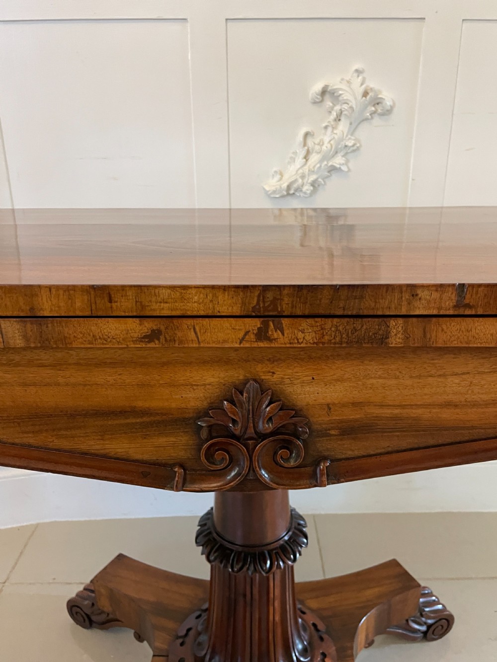 A Victorian rosewood fold-over card table featuring a turned central pedestal, carved frieze, and a quadform base with scroll feet. View XII