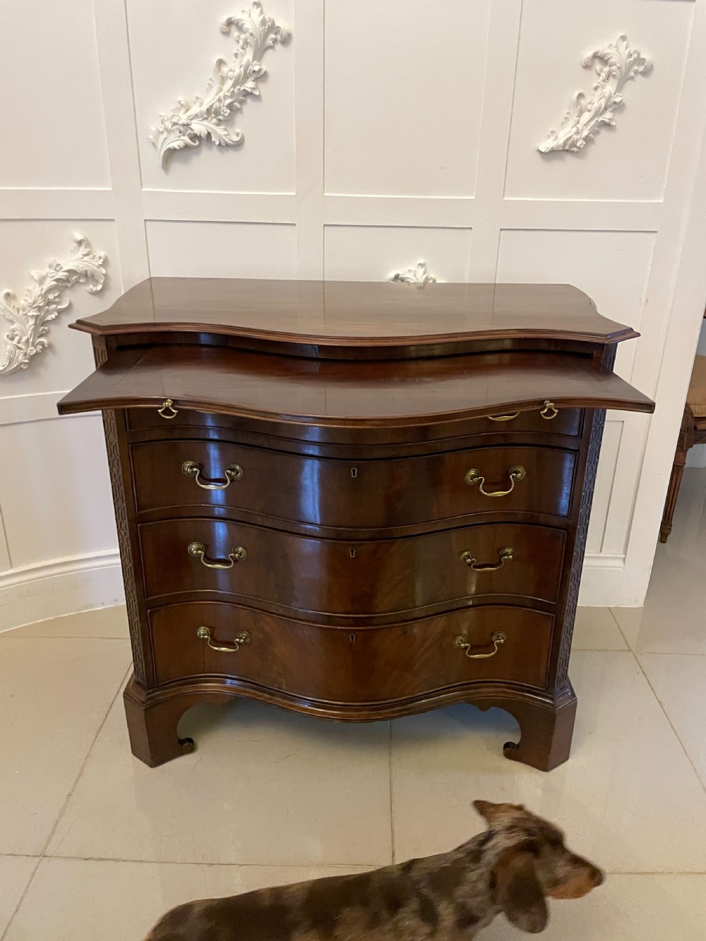 An Edwardian mahogany chest of drawers with a serpentine curved front, four graduated drawers, brass swan-neck handles, and bracket feet. View V