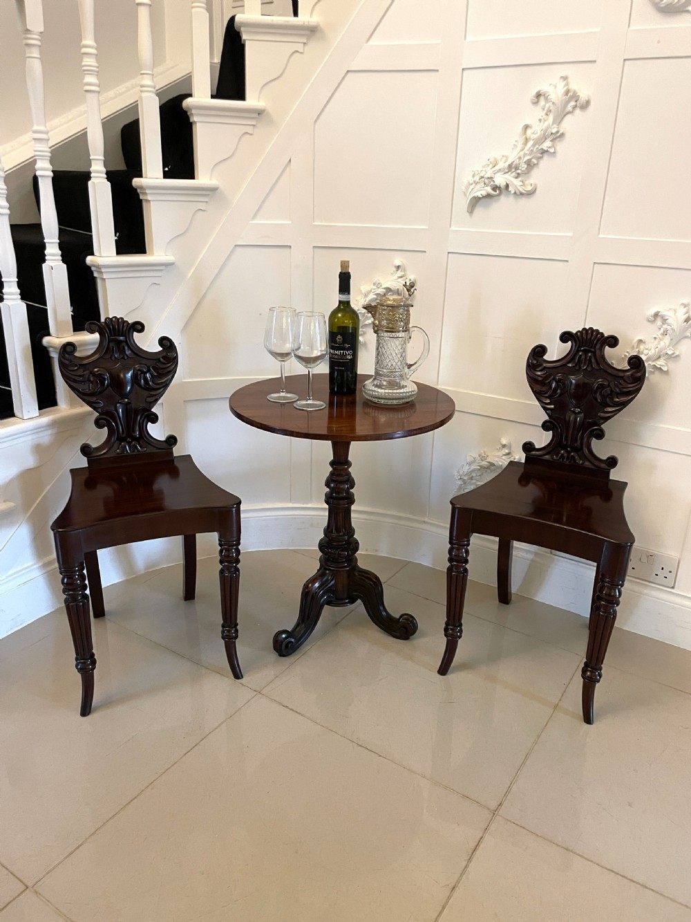 A pair of dark mahogany Regency hall chairs featuring intricate carved cartouche backs, shaped solid wooden seats, and turned, reeded front legs. View II