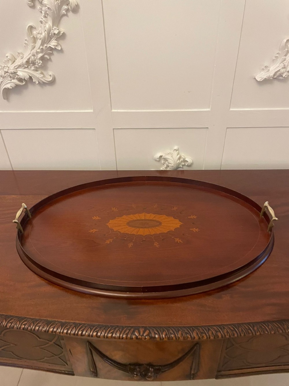 An oval Edwardian mahogany tea tray featuring intricate satinwood inlay and fitted brass handles.