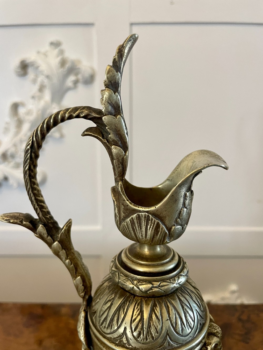 A matching pair of ornate Victorian brass ewers with decorative scroll handles, leaf motifs, and footed bases resting on a polished timber surface. View VII