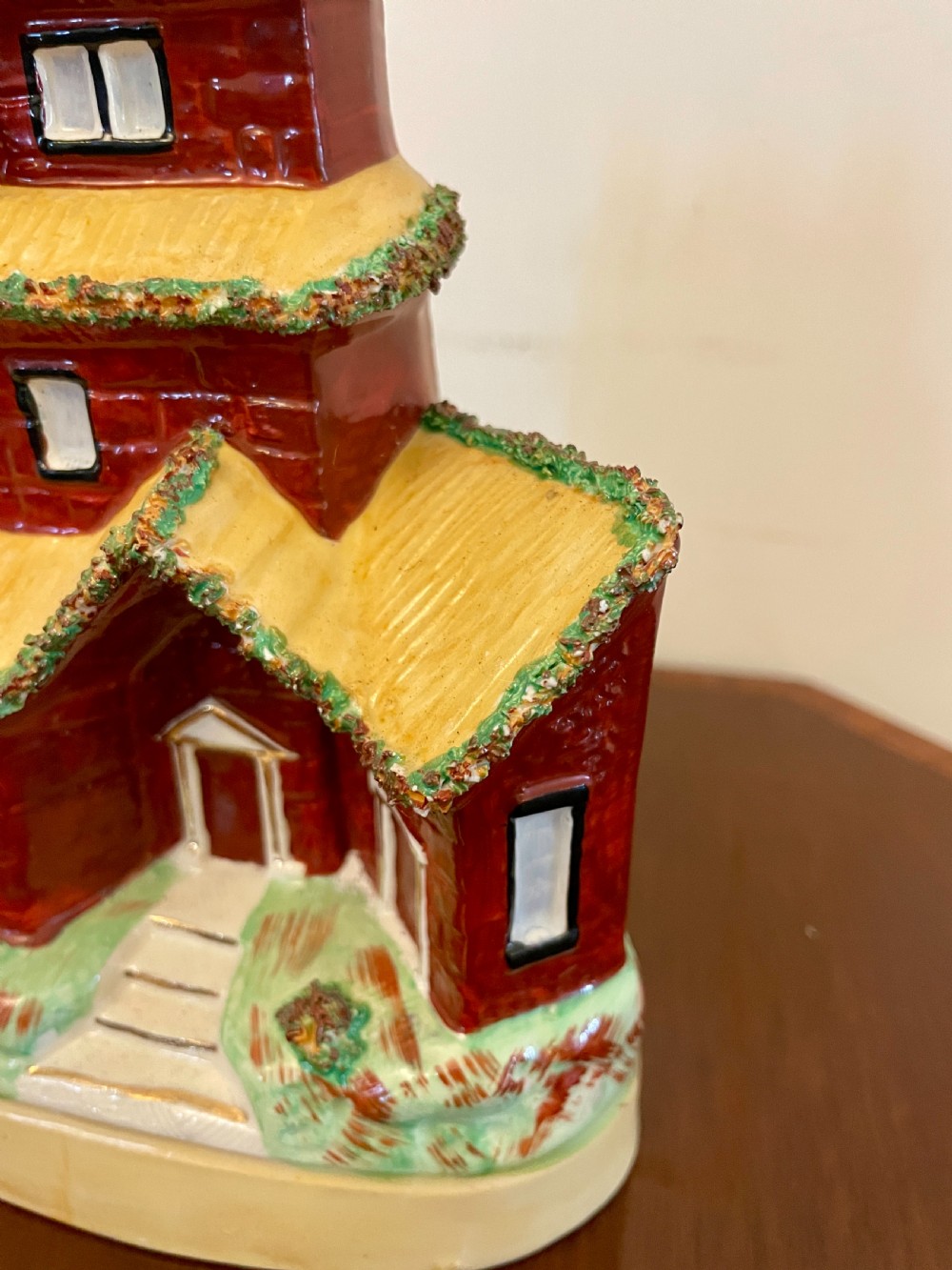 A Victorian Staffordshire pottery flatback figurine depicting a multi-storey terracotta red house with a yellow thatched roof, green encrusted foliage trim, and two chimneys. View II